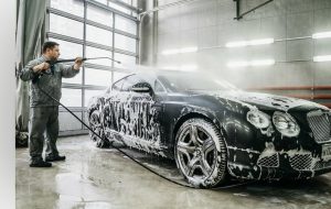 Um Profissional em um lava-rápido usa uma mangueira de alta pressão para aplicar sabão em um carro preto luxuoso.