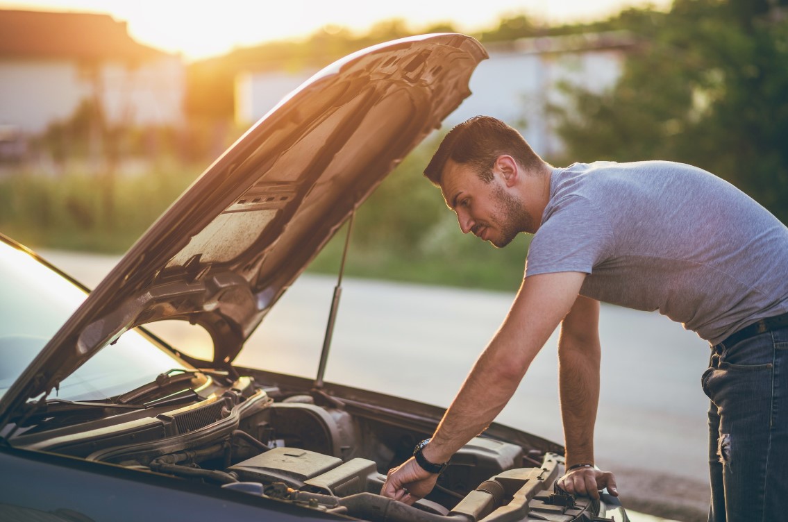 Homem inspecionando o motor de um carro com o capô aberto.