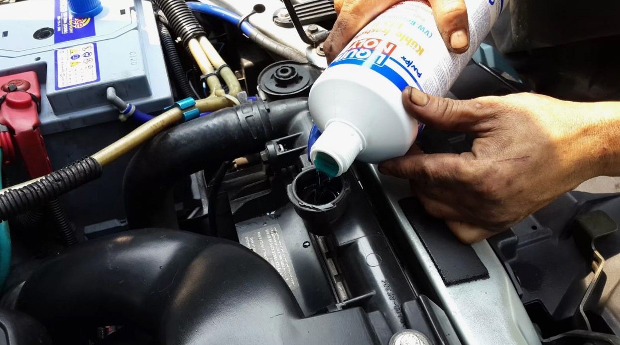 Pessoas despejando aditivo azul no radiador de um carro.